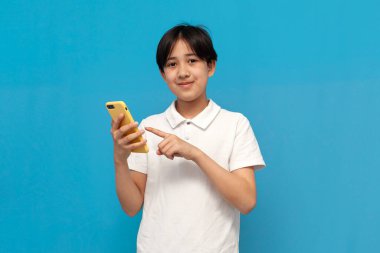 Beyaz tişörtlü Asyalı çocuk mavi arka planda akıllı telefon kullanıyor. Telefonda Koreli çocuk tipleri var.