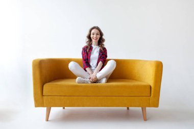 Genç tatlı kız yumuşak rahat kanepeye oturur ve gevşer, tembel kadın dinlenir ve sarı kanepeye uzanır beyaz izole arka planda.