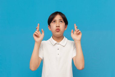 Asyalı çocuk şans diliyor, şans diliyor ve mavi izole edilmiş geçmişe inanıyor, Koreli beyaz tişörtlü çocuk endişeleniyor ve hayaller kuruyor.