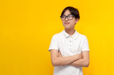 12 yaşındaki Asyalı, gözlüklü, beyaz tişörtlü, kolları çapraz duran ve sarı arka planda duran zeki çocuk Koreli çocuk fotokopi odasına bakıyor.