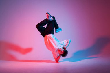 Genç erkek dansçı neon ışıkta dans ediyor, erkek akrobat kırmızı arka planda dans ediyor, hip hop sanatçısı hareket ediyor ve elleri üzerinde duruyor.