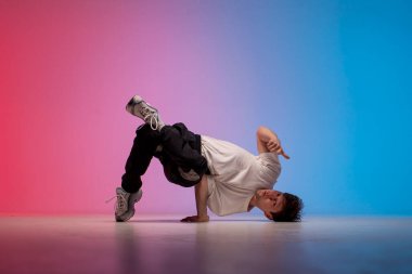 Genç erkek dansçı neon ışıkta dans ediyor, erkek akrobat kırmızı arka planda dans ediyor, hip hop sanatçısı hareket ediyor ve elleri üzerinde duruyor.