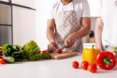 Önlüklü Afro-Amerikan adam mutfakta domates kesiyor, yakın plan, çok ırklı çift sebze ve sebzeli sağlıklı bir sebze salatası hazırlıyor.