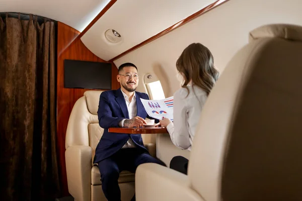 stock image business people are discussing deal in private luxury jet, asian businessman in suit is talking to female colleague in airplane, korean boss is at meeting with client