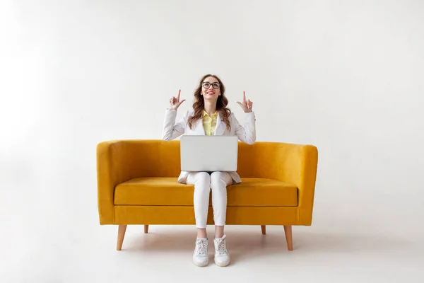 スーツ姿の若い実業家は快適なソファの上にラップトップを使用し コピースペースに表示され 正式な服の女の子は白い隔離された背景に黄色のソファの上にコンピュータに入力しています — ストック写真