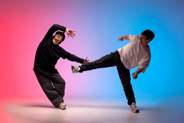 two dancer guys break dance on red blue background and do trick together, male acrobats perform pair dance in neon lighting, hiphop performers