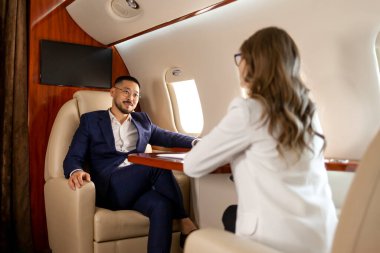 Özel uçaktaki iş adamları, takım elbiseli Asyalı işadamı bayan meslektaşlarıyla iş görüşmeleri, yöneticiler grafikleri ve raporları patrona gösteriyor, iş ortakları jet ile uçuyor.
