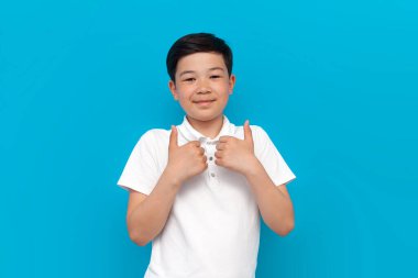 Beyaz tişörtlü küçük Asyalı çocuk mavi arka planda beğeniler gösteriyor Koreli çocuk izole edilmiş arka planda tavsiye jesti gösteriyor.