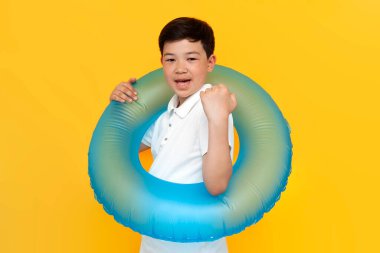 On yıllık Asyalı, şişme yüzme yüzüklü küçük çocuk sarı izole edilmiş arka plana karşı zaferle seviniyor. Yazın Koreli çocuk başarıyı ve iyi şansı kutluyor.