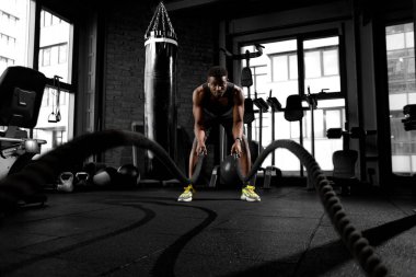 Genç atletik Afrikalı Amerikalı adam, spor salonunda iplerle antrenman yapıyor. Spor salonunda motivasyonlu bir adam, spor salonunda ip sallıyor.