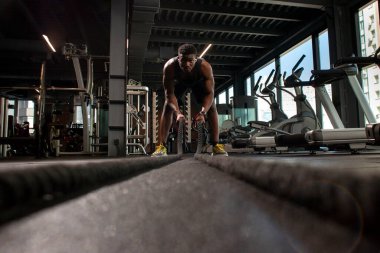 Genç atletik Afrikalı Amerikalı adam, spor salonunda iplerle antrenman yapıyor. Spor salonunda motivasyonlu bir adam, spor salonunda ip sallıyor.