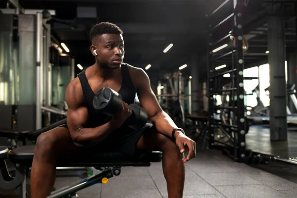 stock image young athletic african american man trains in dark gym, athletic guy lifts heavy dumbbells in fitness club