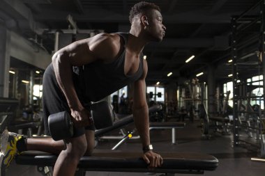 Genç atletik Afrikalı Amerikalı adam koyu renk spor salonunda antrenman yapıyor, atletik adam spor salonunda halterleri kaldırıyor.