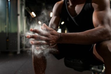 Sportif Afro-Amerikan erkek, ellerini magnezyumla ovalıyor. Spor salonunda ellerini çırpıyor. Toz ve unu yakın çekimde, sporcunun elleriyle.