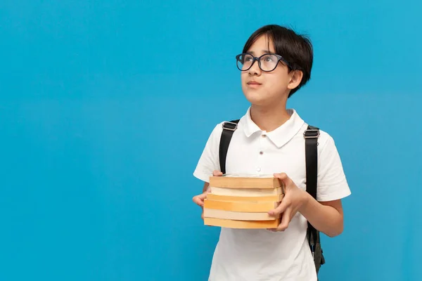 12岁的亚洲男孩 戴着眼镜 背着背包 拿着很多关于蓝色孤立背景的书 韩国孩子回到学校学习和学习 — 图库照片
