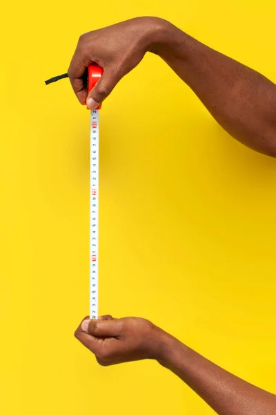 stock image hands of african american man hold tape measure and measure the distance on yellow isolated background, guy with construction measuring tool, close-up