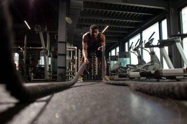 Genç atletik Afrikalı Amerikalı adam, spor salonunda iplerle antrenman yapıyor. Spor salonunda motivasyonlu bir adam, spor salonunda ip sallıyor.