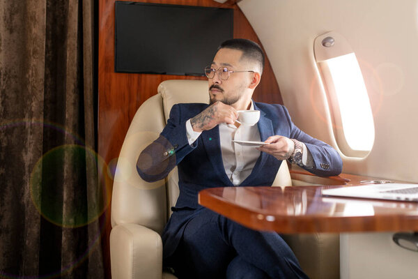 successful Asian businessman in suit and glasses flies in private luxury plane and drinks coffee, Korean trader financier entrepreneur in airplane, luxury lifestyle