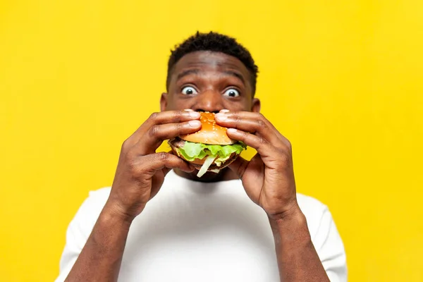Beyaz Tişörtlü Afrikalı Bir Adam Hamburgeri Isırır Sarı Izole Edilmiş — Stok fotoğraf