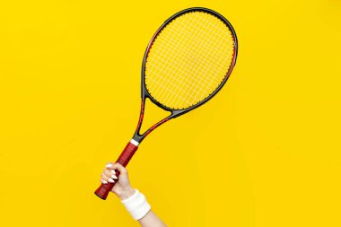 Kadın eli tenis raketini sarı izole bir arka planda tutuyor, spor ekipmanları, yakın plan.