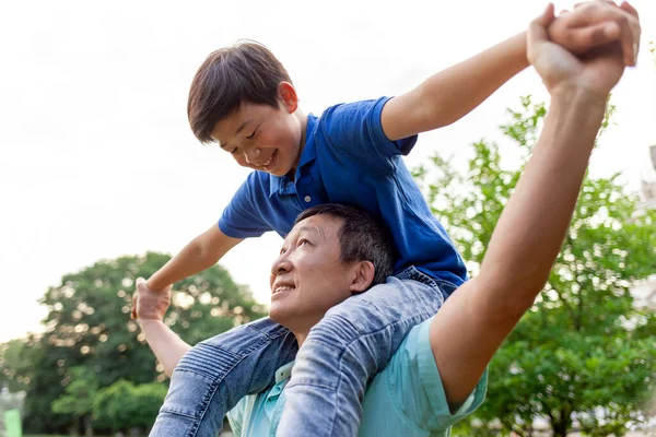 stock image asian boy flying forward on dad's back in summer, korean senior pensioner playing with child in summer outdoors, grandfather carrying grandson