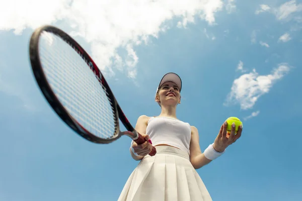 白いユニフォームの女子テニス選手がテニスコートでラケットとボールを持ち女性アスリートが空に向かって屋外でテニスをする — ストック写真