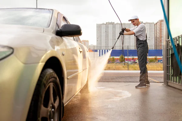 Młody Facet Mundurze Myjnia Samochodowa Myje Samochód Wodą Węża Mężczyzna — Zdjęcie stockowe