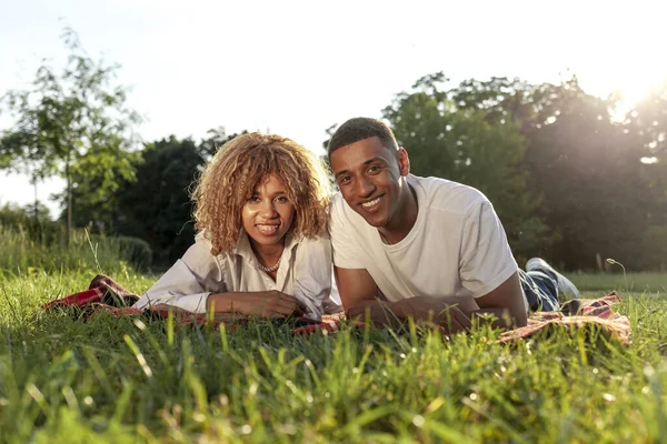 アフリカ系アメリカ人の若いカップルが夏の公園に草と笑顔で横たわっています男と女は自然にリラックスしています — ストック写真