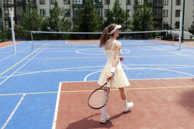Tenis kortunda raket tutan beyaz üniformalı genç kız tenisçi, dışarıda tenis oynayan bayan sporcu.
