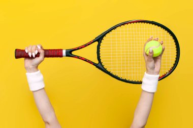 Kadın elleri tenis raketi ve tenis topunu sarı izole arka planda, spor ekipmanları, yakın çekim