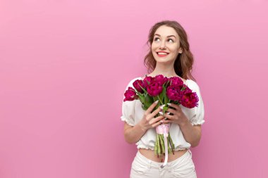 Beyaz elbiseli genç ve çekici bir kız pembe lale buketini tutuyor ve fotokopi odasına bakıyor.