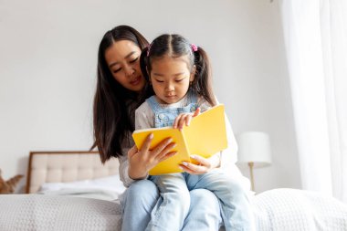 Asyalı bir aile evde oturup kitap okuyor Koreli bir anne küçük kızına okuma yazma öğretiyor.