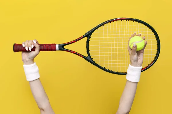 黄色い隔離された背景にテニスラケットとテニスボールを持ち上げ保持する女性の手 スポーツ用具 クローズアップ — ストック写真