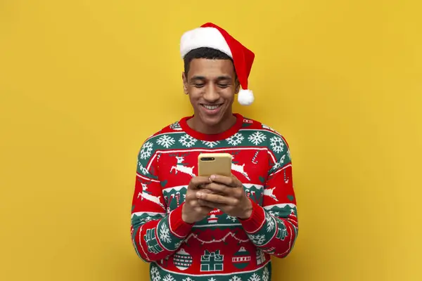 크리스마스 모자를 아프리카 미국인 남자가 스마트폰을 사용하고 노란색외진 배경에 미소를 — 스톡 사진