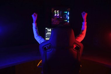gamer plays a computer game at night and celebrates a victory, the player sits in a comfortable computer chair with his hands up, victory gesture
