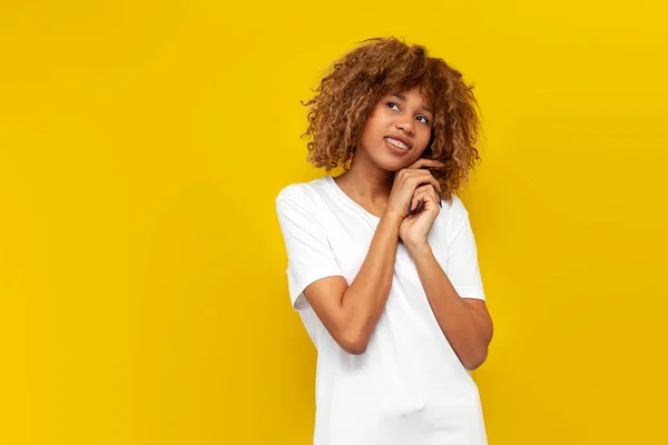 Stock image young curly american girl with braces shy and dreaming over yellow isolated background, african woman with hairstyle smiles and presents looking at copy space