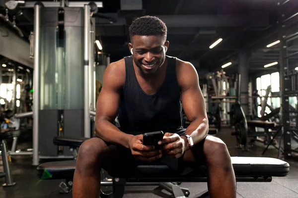 Jovem Atlético Homem Americano Africano Senta Ginásio Escuro Usa Smartphone — Fotografia de Stock