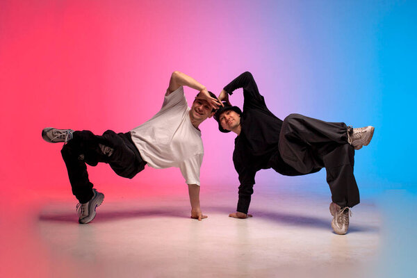 two dancer guys break dance on red blue background and do trick together, male acrobats perform pair dance in neon lighting, hiphop performers