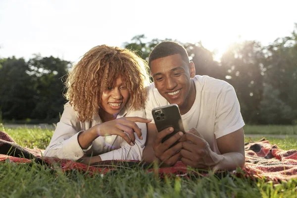 アフリカ系アメリカ人の若いカップルは夏に公園にあり スマートフォンを使用しています — ストック写真
