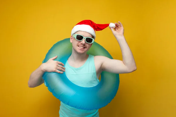 young guy in a New Year\'s hat in the summer on vacation with an inflatable swim ring rejoices and smiles, a man with a swim ring for Christmas