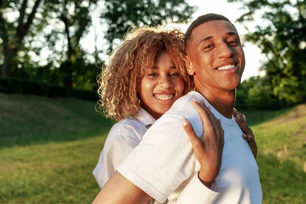 幸せな若いアフリカ系アメリカ人のカップル一緒に公園に立って抱きかかえている彼女のボーイフレンドと笑顔 愛とケアの概念 — ストック写真
