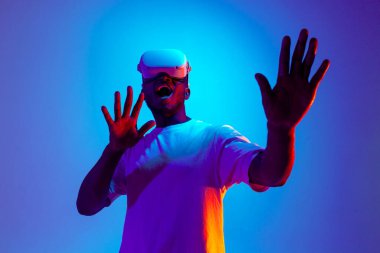 Sanal gerçeklik gözlüklü Afro-Amerikan erkek oyuncu neon ışıklı ellere dokunuyor, korkmuş adam modern VR cihazları kullanıyor ve çığlıklar atıyor.