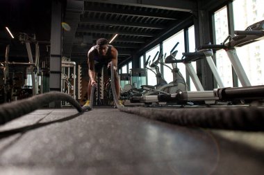 Genç atletik Afrikalı Amerikalı adam, spor salonunda iplerle antrenman yapıyor. Spor salonunda motivasyonlu bir adam, spor salonunda ip sallıyor.