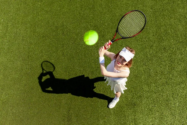 白いスポーツの若い女の子のテニス選手は緑のコートでテニスをし テニスラケットを持つ女性コーチは空気中のボールを打つ トップビュー — ストック写真