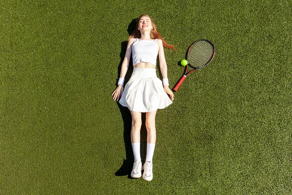 身穿白色运动服 头戴网球拍的年轻女子网球选手躺在绿场 复制空间 — 图库照片
