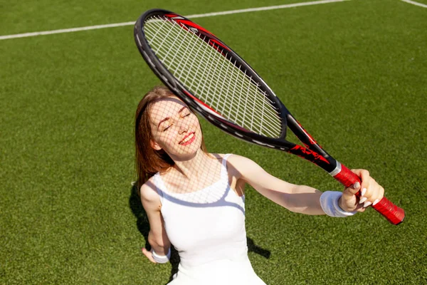 テニスラケットのある白いスポーツで若い女の子のテニス選手が座っていると緑の裁判所に残り 女性コーチの笑顔 — ストック写真