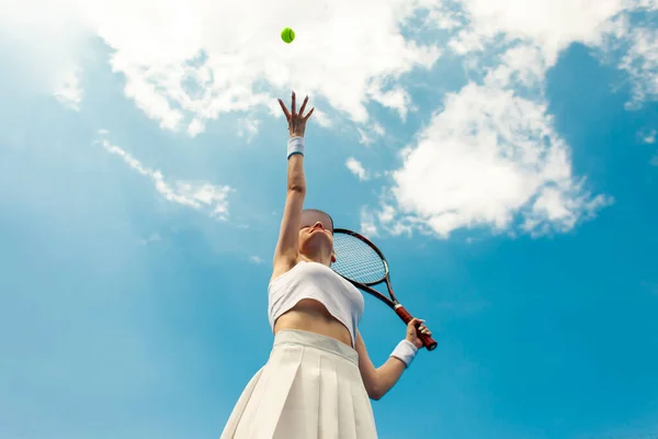 白い制服の女子テニス選手はラケットを持ってテニスコートにボールを投げ 女子アスリートは空に対して屋外でテニスをする — ストック写真