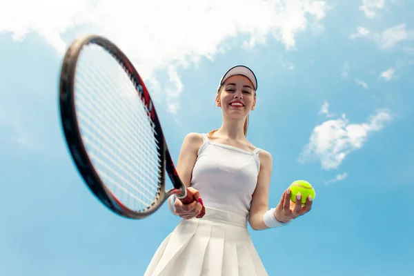白いユニフォームの女子テニス選手がテニスコートでラケットとボールを持ち女性アスリートが空に向かって屋外でテニスをする — ストック写真
