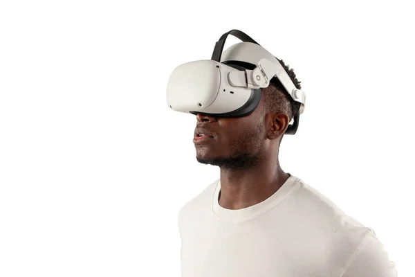 Stock image serious african american man in white t-shirt looks away in virtual reality glasses on white isolated background, guy in vr glasses looks at copy space