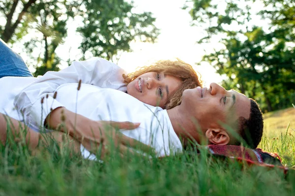 african american romantic young couple lies on the grass in the park and sleeps in nature, happy family rests and dreams outdoors, woman hugs her boyfriend and smiles